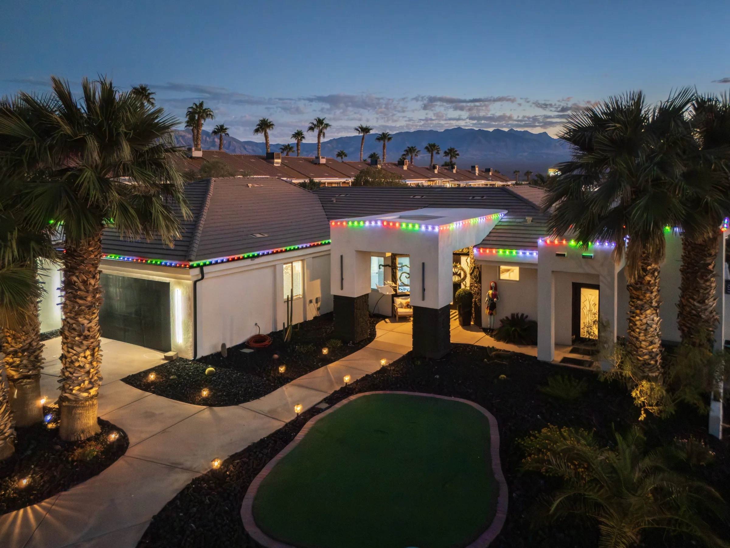 A GLOMO install at dusk: desert home with multicolor permanent lights along the roofline, palms and a putting green out front
